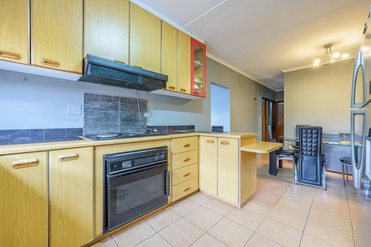 A functional kitchen featuring light wood cabinetry, built-in oven and hob, extractor fan, and tiled flooring, with an open-plan layout leading to the dining area.