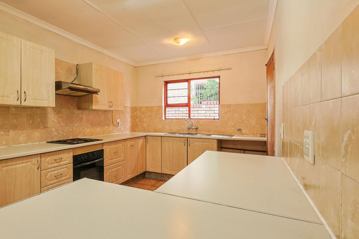 A functional kitchen featuring light wood-tone cabinetry, laminate countertops, a built-in oven with hob, and neutral ceramic wall and floor tiling.