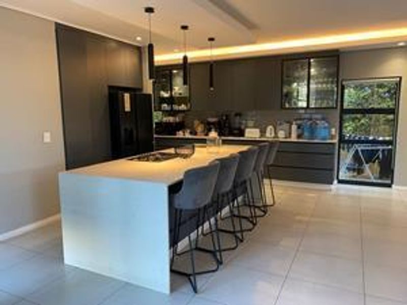 Modern kitchen featuring a large central island with a built-in hob, sleek dark cabinetry, and contemporary pendant lighting.