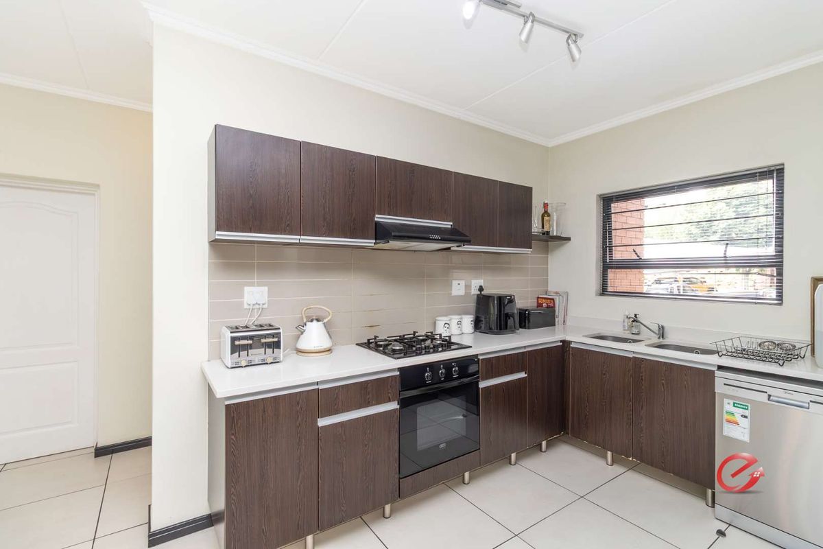 A functional kitchen featuring dark wood-grain cabinetry, light countertops, a built-in gas hob, oven, extractor fan, and tiled flooring.
