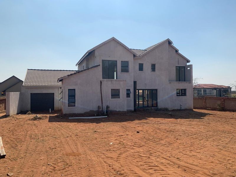 Rear view of a double-storey residential property under construction, featuring a tiled roof, garage, and unfinished exterior walls set on a large plot.