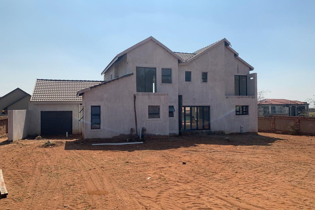 Rear view of a double-storey residential property under construction, featuring a tiled roof, garage, and unfinished exterior walls set on a large plot.