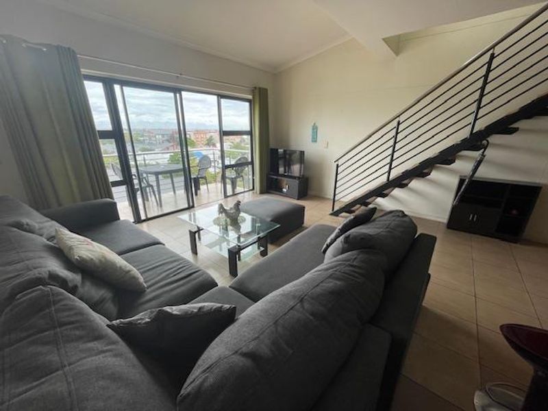 Spacious living room featuring tiled flooring, a metal staircase, and large sliding glass doors leading to an outdoor balcony area.