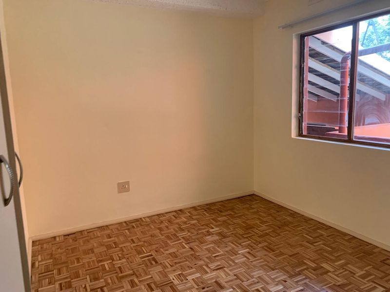 An empty bedroom featuring classic parquet flooring, a built-in cupboard, and a louvered window providing natural light.