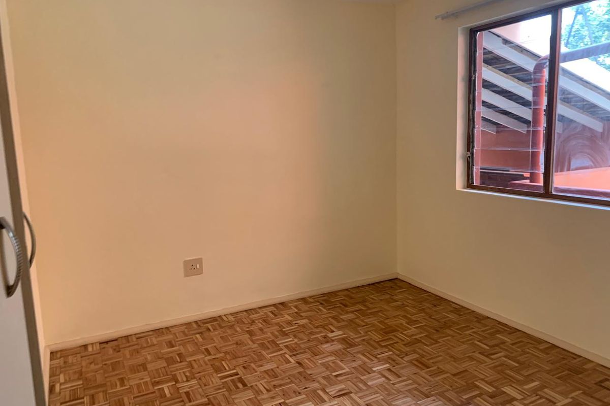 An empty bedroom featuring classic parquet flooring, a built-in cupboard, and a louvered window providing natural light.
