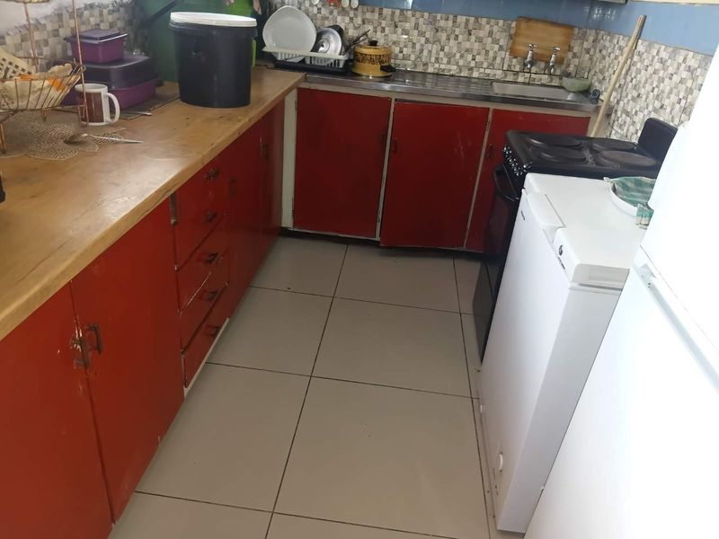 A compact kitchen featuring tiled flooring, a stainless steel sink, tiled splashback, and dated red cabinetry with a wooden countertop.