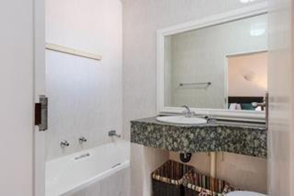 A functional bathroom featuring a built-in bathtub with wall-mounted fixtures and a vanity with a stone-look countertop and large wall mirror.