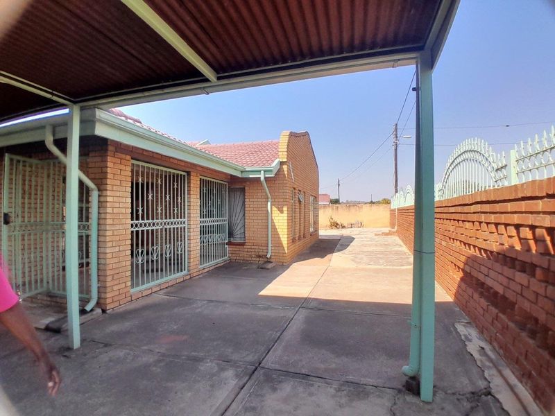 Rear exterior view of a face brick house featuring a paved courtyard, metal carport structure, and secure window bars.