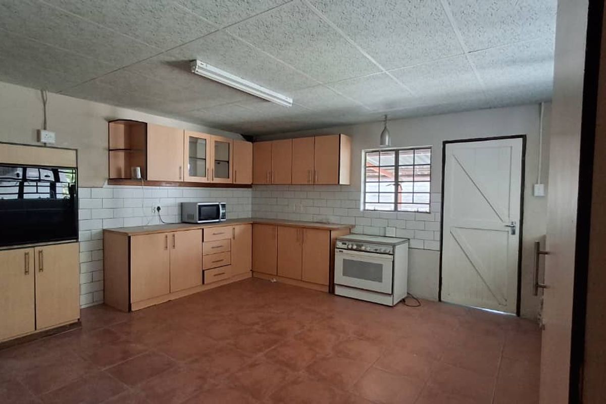 A functional kitchen featuring light wood cabinetry, tiled splashbacks, a freestanding stove, and tiled flooring with direct access to an exterior door.