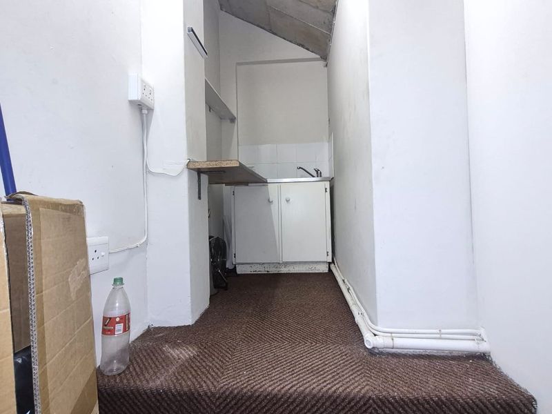 A small, utilitarian scullery or kitchenette area featuring basic built-in cabinetry, a sink, and exposed plumbing, requiring cosmetic updates and flooring replacement.