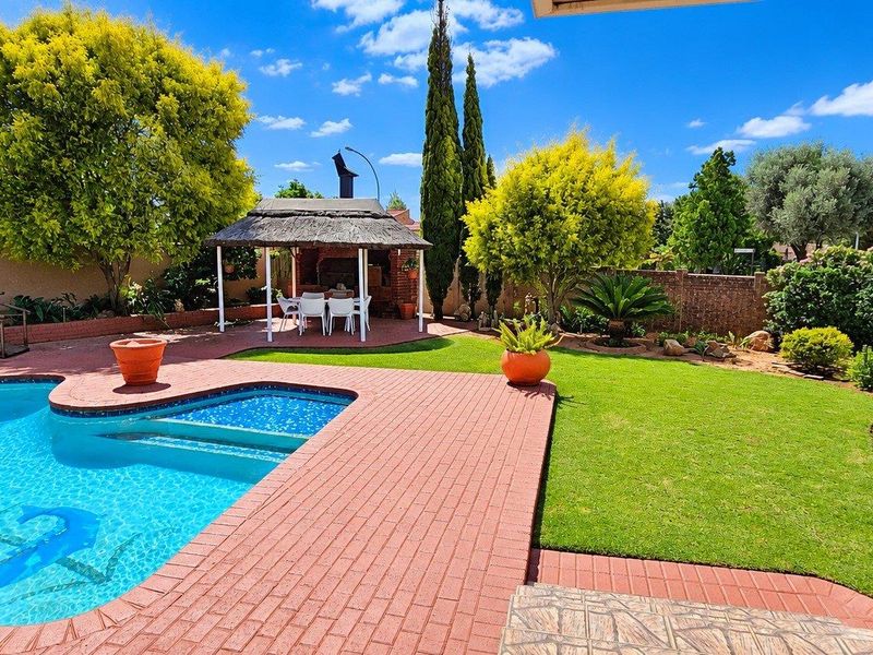 Well-maintained outdoor entertainment area featuring a swimming pool, brick-paved patio, and a thatched gazebo set within a landscaped garden.