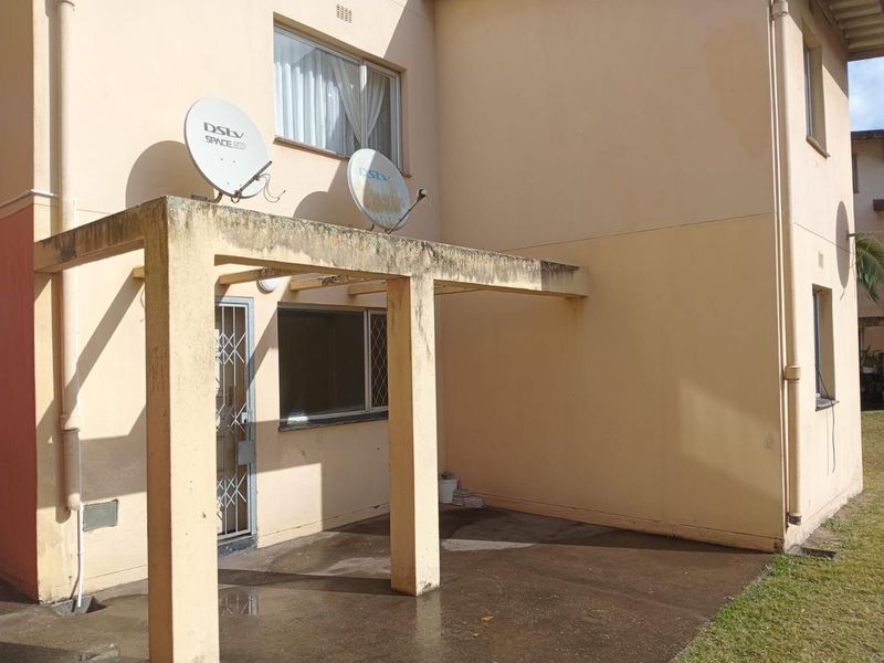 Rear exterior view of the apartment featuring a concrete pergola structure, security gate, and satellite dish installation on the building facade.