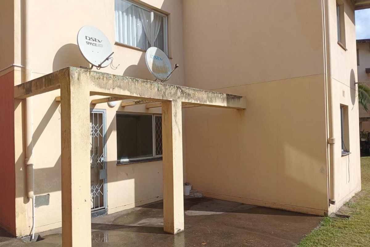 Rear exterior view of the apartment featuring a concrete pergola structure, security gate, and satellite dish installation on the building facade.