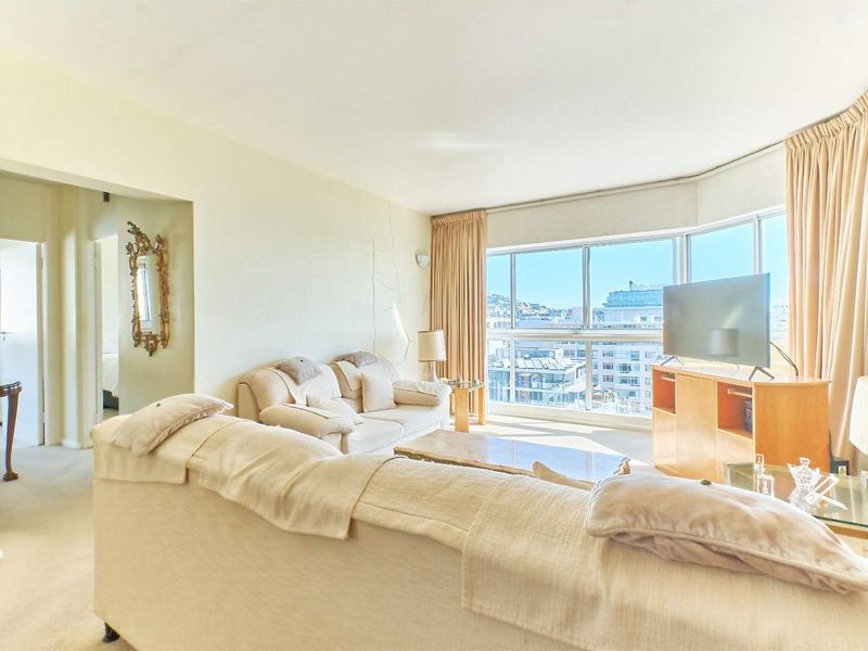 A bright living room featuring a large bay window with city views, carpeted flooring, and neutral wall finishes.