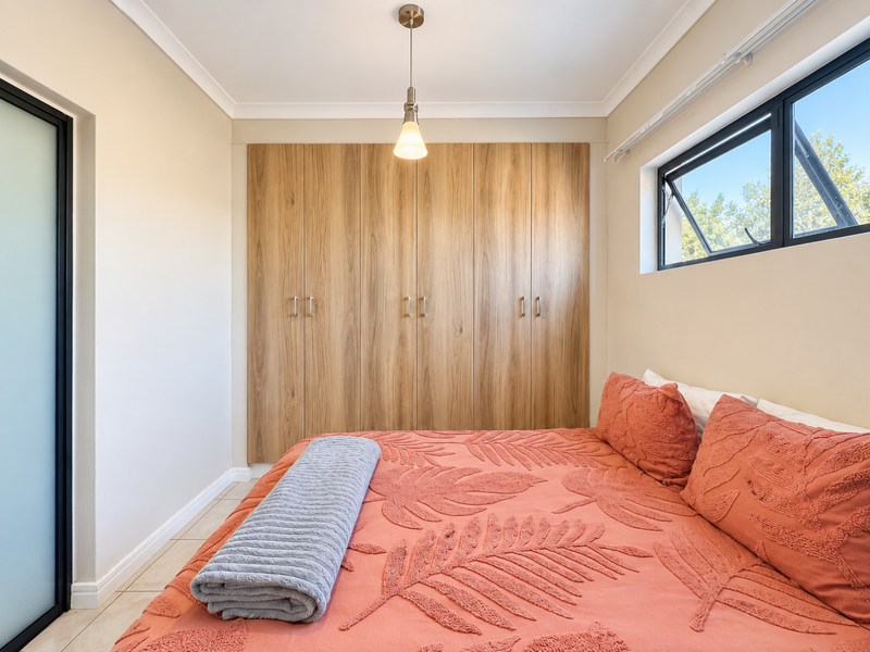 A well-maintained bedroom featuring built-in wooden cupboards, tiled flooring, and a modern pendant light fixture, offering a clean and functional living space.