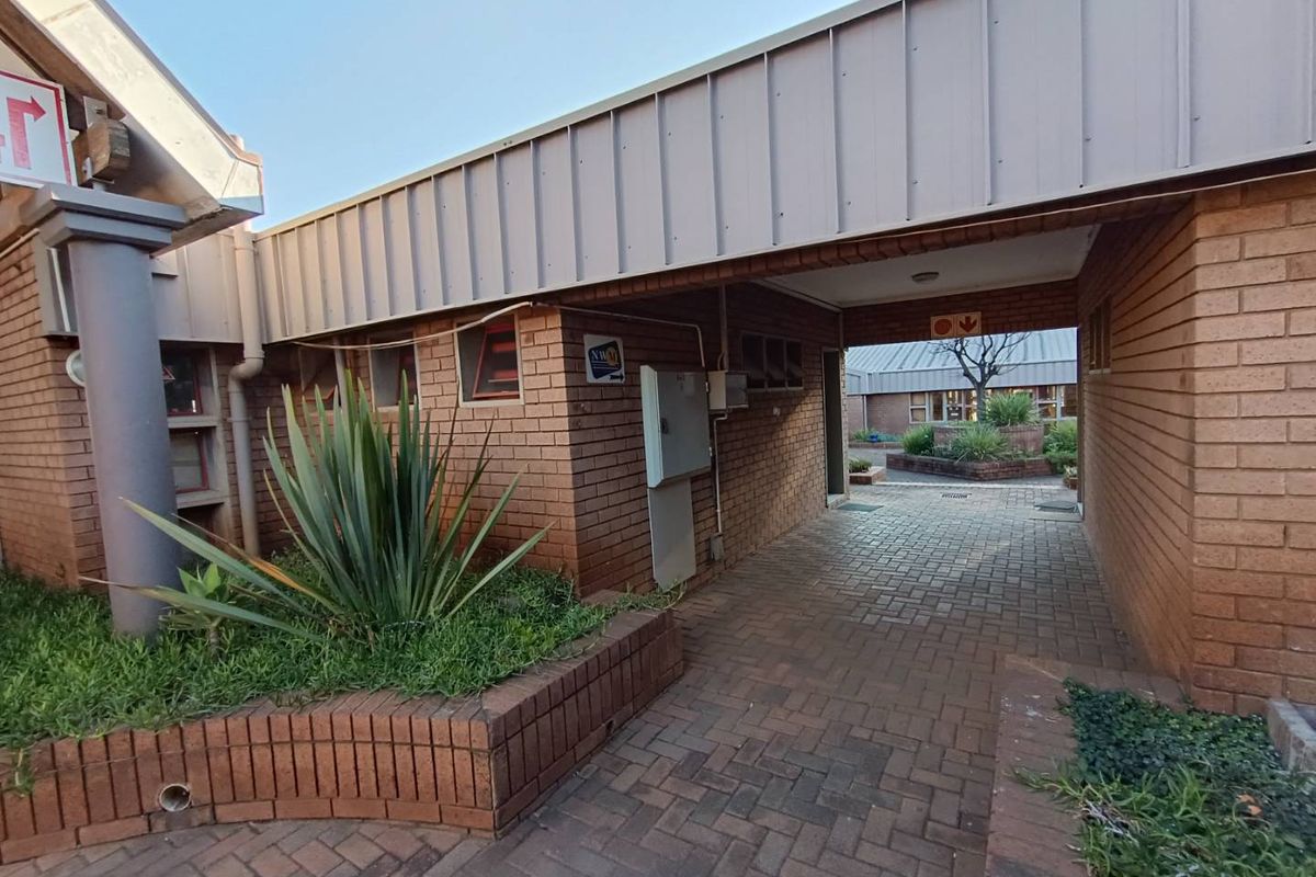 A covered brick walkway providing access between building sections, featuring paved flooring and integrated brick planter boxes.