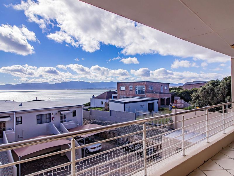A spacious covered balcony featuring tiled flooring and a metal balustrade, offering expansive coastal and mountain views.