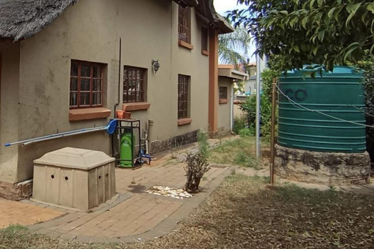 Rear view of a traditional thatched-roof house featuring a paved walkway, garden space, and a large water storage tank.