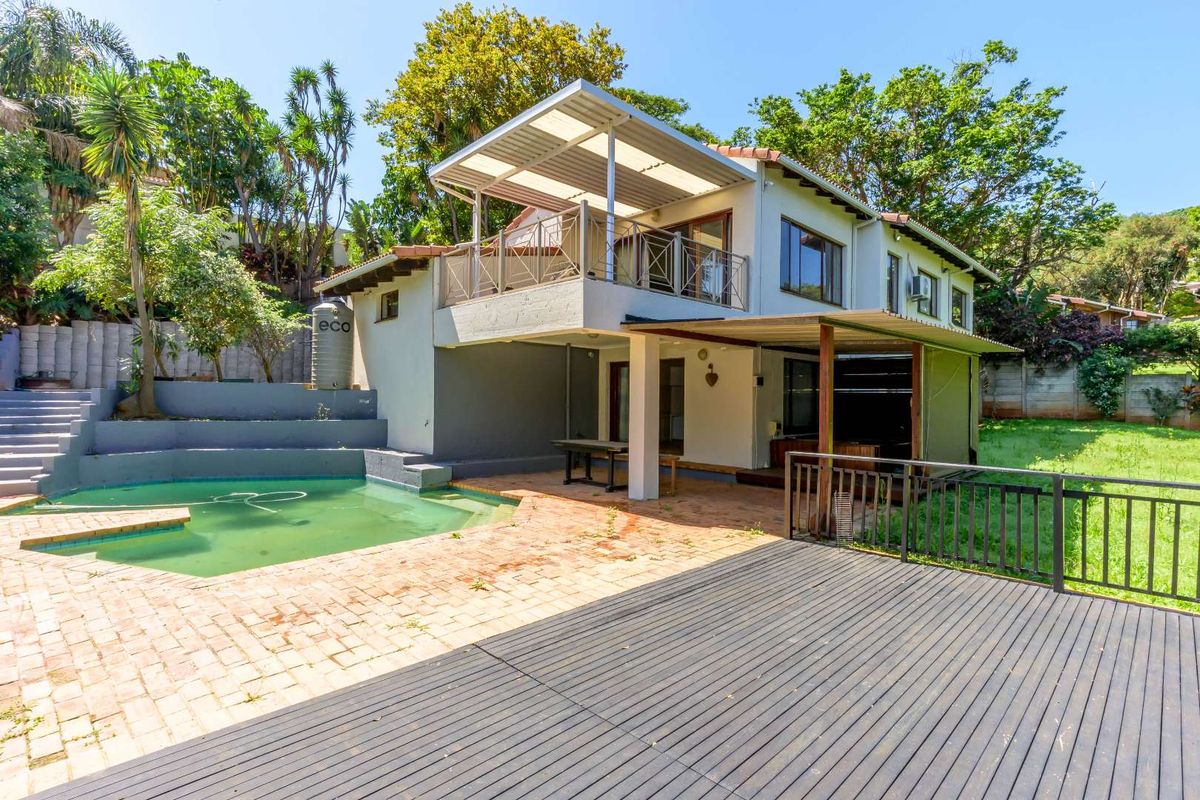 Rear view of the property featuring a swimming pool, paved patio area, elevated balcony with metal railing, and a timber deck.