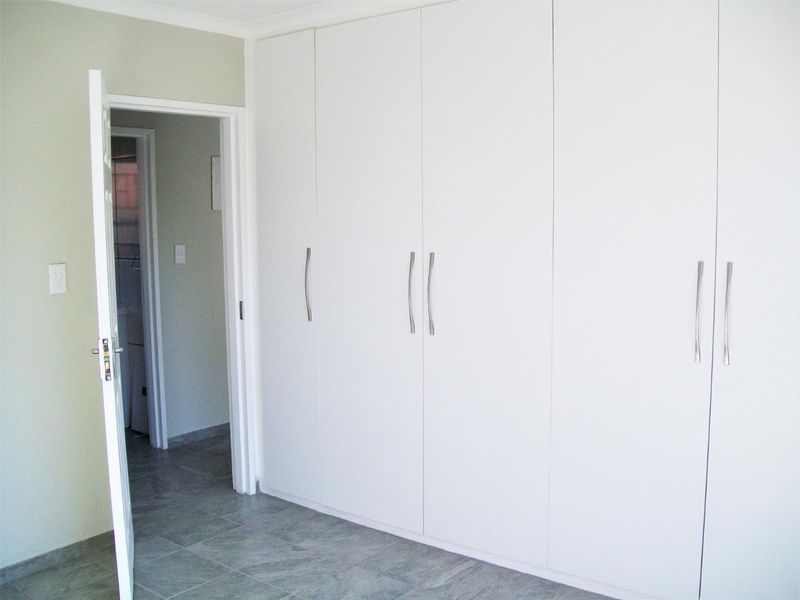 A clean, empty bedroom featuring neutral tiled flooring and extensive floor-to-ceiling built-in cupboards with modern handles.