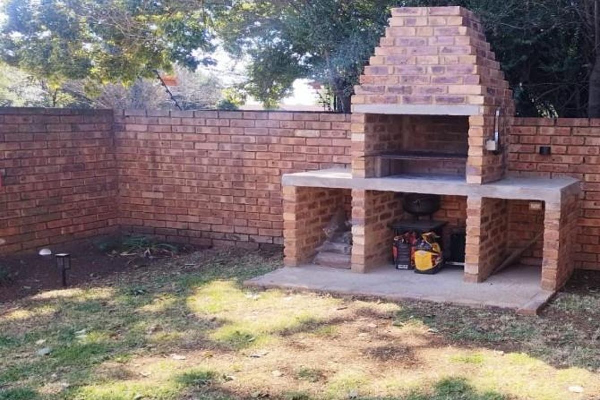 A private rear garden area featuring a built-in brick braai with a concrete countertop, enclosed by a solid brick boundary wall.