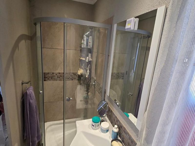 A functional bathroom featuring a corner shower enclosure, vanity basin, and wall-mounted mirror with neutral tiled finishes.