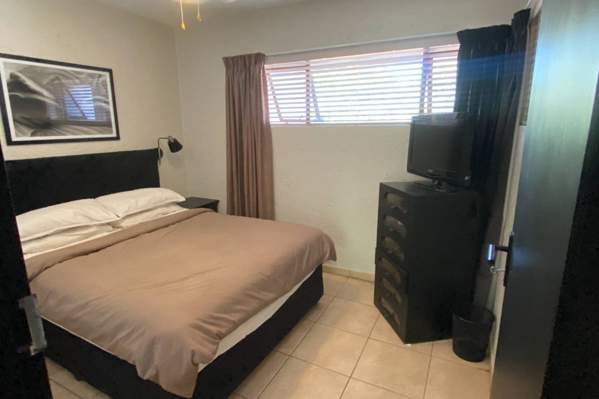 A functional bedroom featuring tiled flooring, a ceiling fan, and a window with fitted blinds.