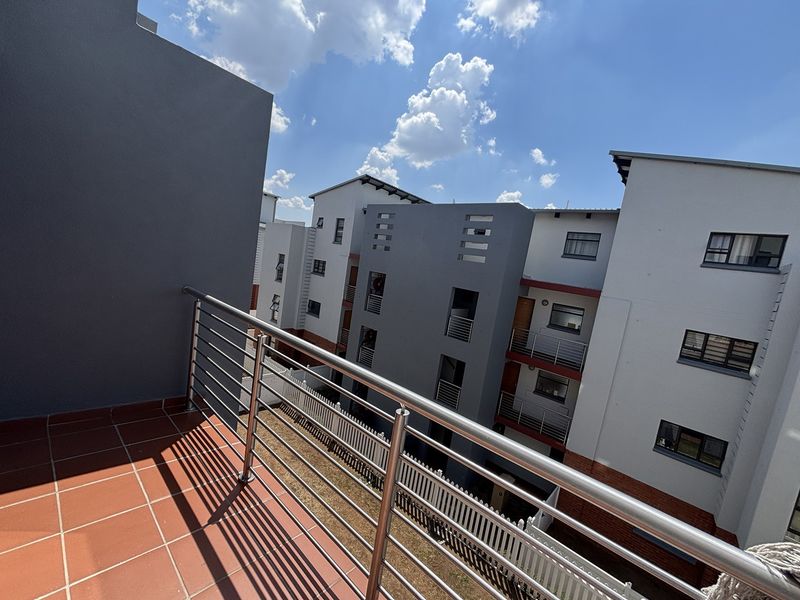 A private balcony featuring tiled flooring and a modern stainless steel balustrade, offering an elevated view of the surrounding apartment complex.
