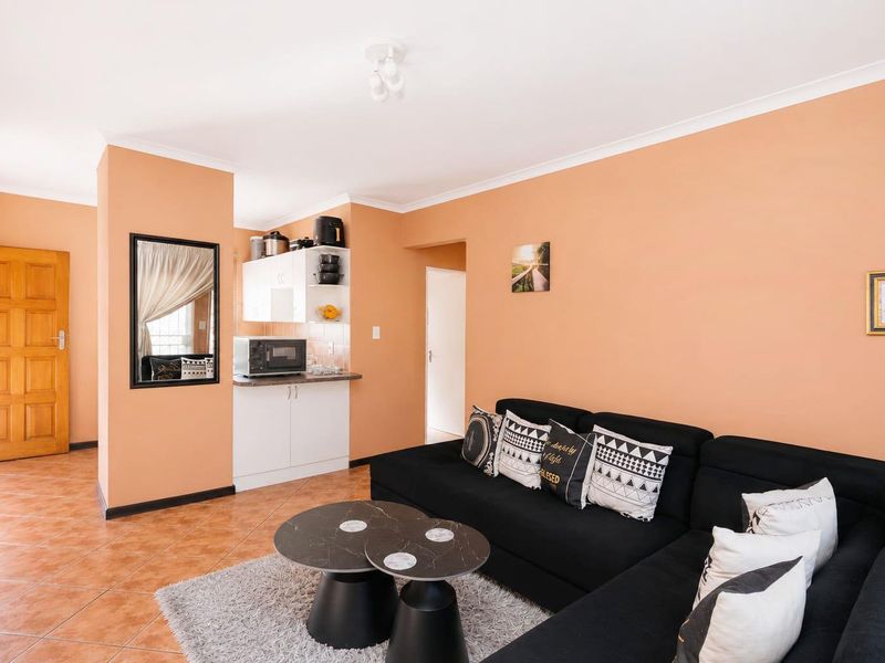 Open-plan living area featuring tiled flooring, a compact kitchen nook with built-in cabinetry, and a solid wood door leading to adjacent spaces.