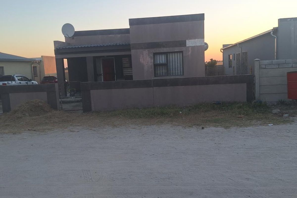Front view of a single-story residential house featuring a boundary wall, security gate, and satellite dish, set against a sunset sky.