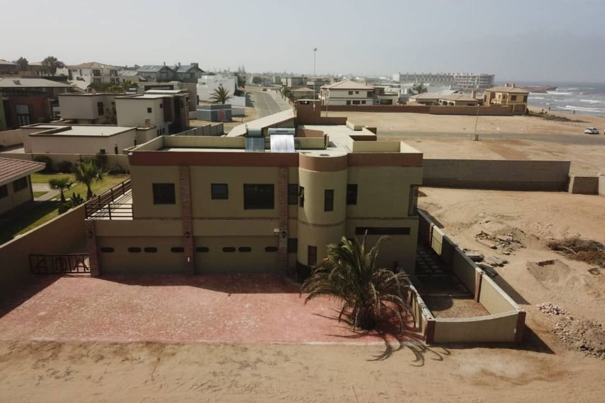 Aerial view of a multi-level coastal property featuring a paved driveway, integrated garage, and rooftop solar water heating system.
