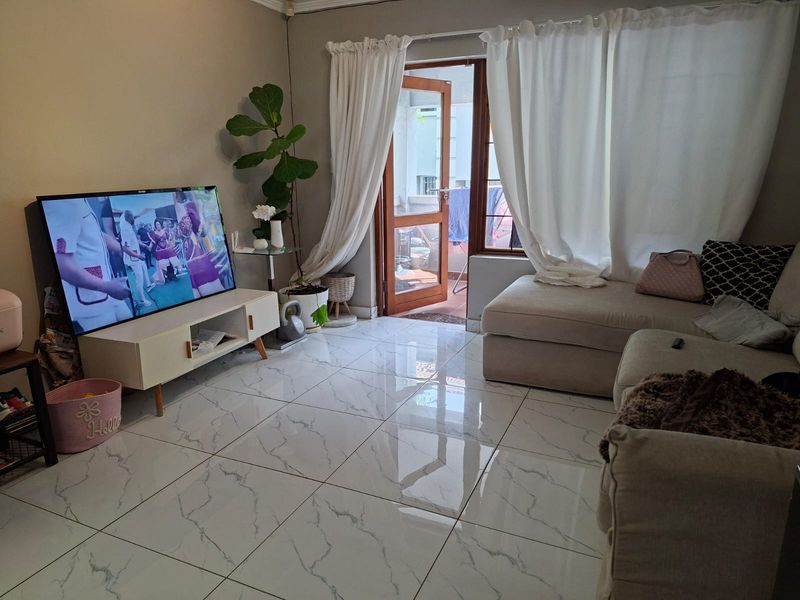 A bright living room featuring polished marble-look floor tiles and direct access to an outdoor balcony through a timber-framed glass door.