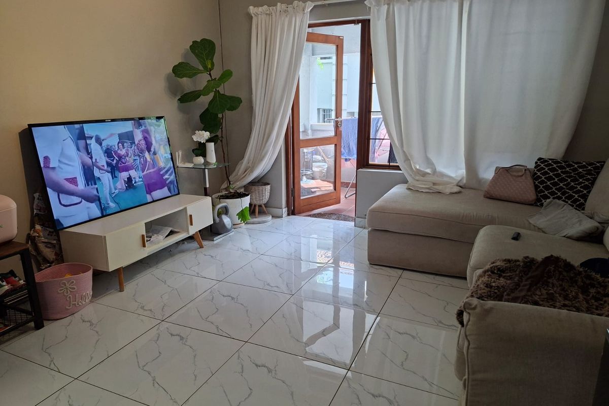 A bright living room featuring polished marble-look floor tiles and direct access to an outdoor balcony through a timber-framed glass door.