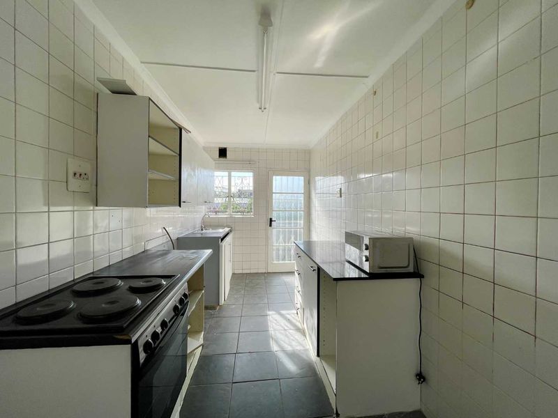 A dated galley-style kitchen featuring tiled walls, built-in cabinetry, and an electric stove, offering significant potential for modernization and renovation.