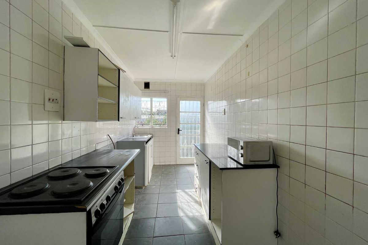 A dated galley-style kitchen featuring tiled walls, built-in cabinetry, and an electric stove, offering significant potential for modernization and renovation.