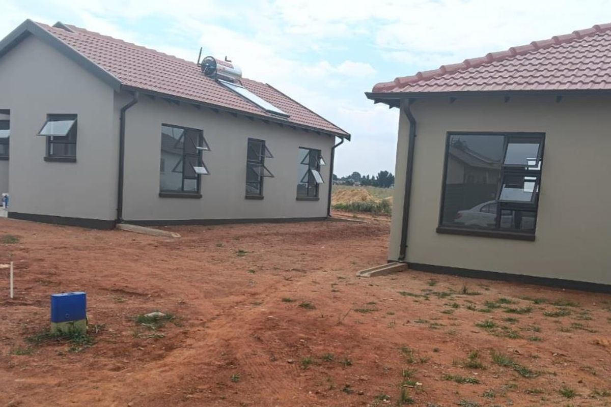 Exterior view of modern residential houses featuring tiled roofs, solar water heating systems, and aluminium window frames in a developing estate.