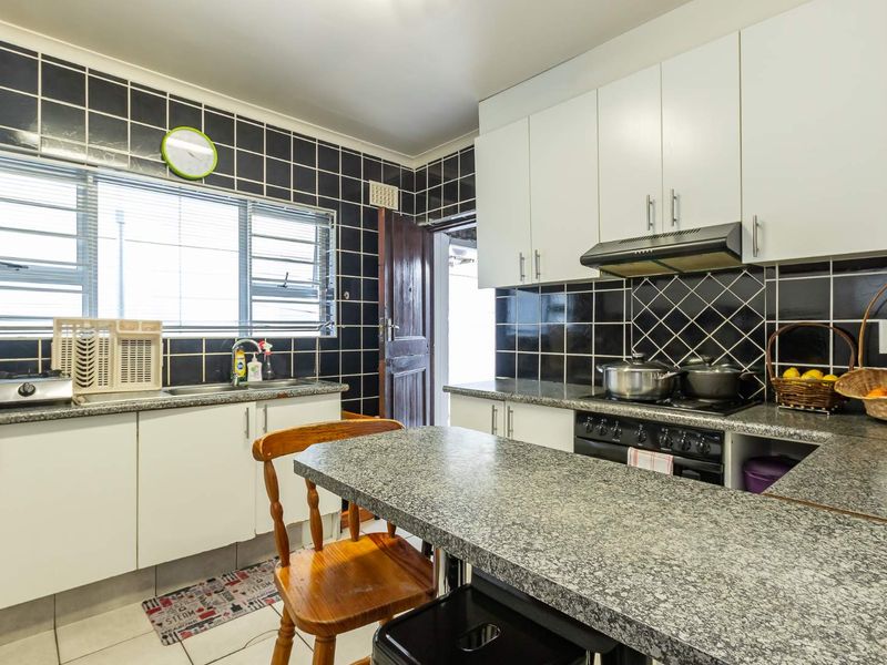 Functional kitchen featuring granite countertops, white cabinetry, a tiled backsplash, and a built-in extractor fan with a breakfast nook area.