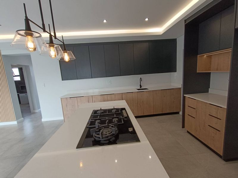Modern kitchen featuring sleek two-tone cabinetry, stone countertops, a central island with a gas cooktop, and recessed lighting.