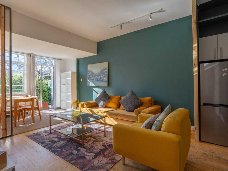 Bright open-plan living area featuring timber flooring, a bold accent wall, track lighting, and direct access to an outdoor space through french doors.