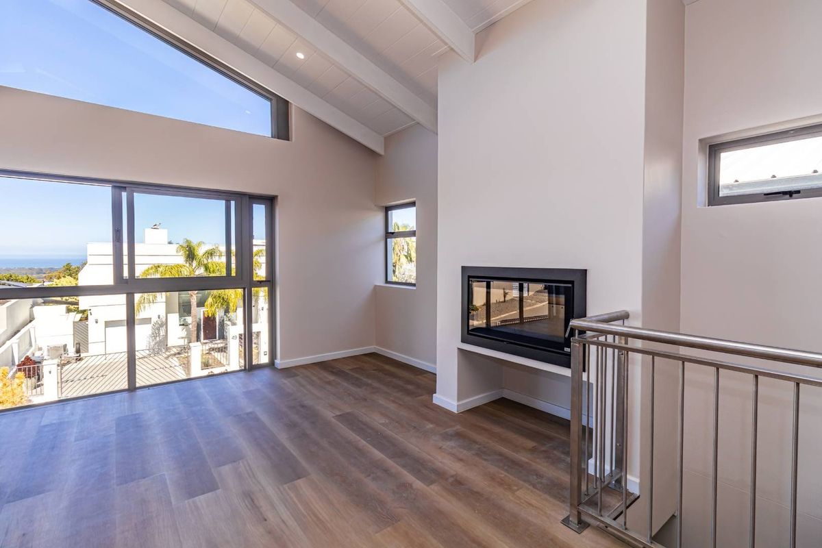 Spacious living area featuring vaulted ceilings with exposed beams, modern laminate flooring, a built-in fireplace, and large sliding glass doors with neighborhood views.