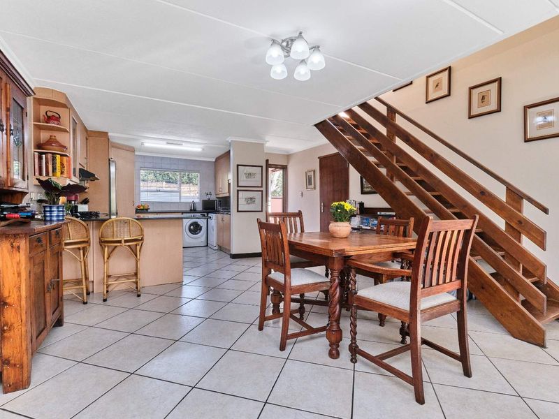Open-plan kitchen and dining area featuring tiled flooring, wooden staircase, and functional built-in cabinetry with integrated kitchen fixtures.