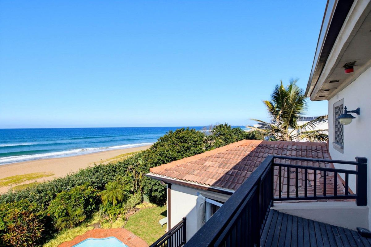 Elevated balcony featuring timber decking and railing, offering expansive views of the coastline, beach, and ocean.