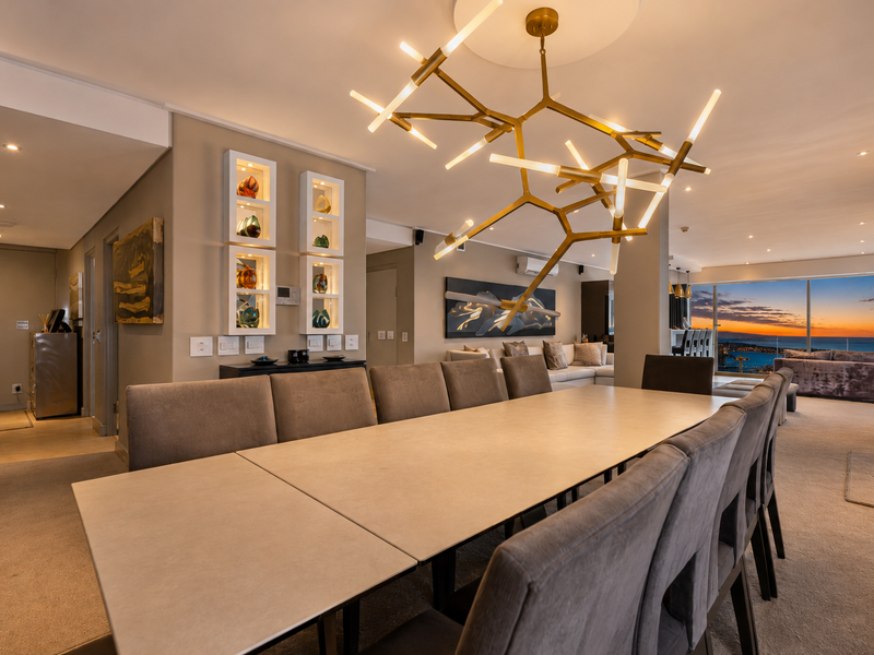 Spacious open-plan dining and living area featuring modern recessed lighting, built-in wall niches, and expansive floor-to-ceiling windows with panoramic sunset views.