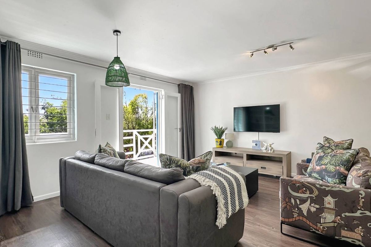 A bright and well-maintained living room featuring laminate flooring, modern track lighting, and direct access to an outdoor balcony through double glass doors.