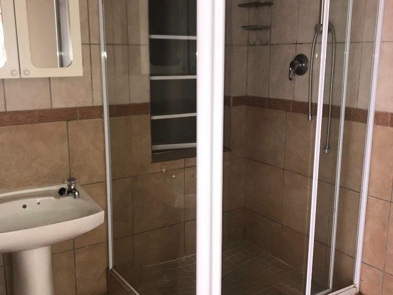 A functional bathroom featuring a pedestal basin, a corner shower enclosure with tiled finishes, and a wall-mounted medicine cabinet.