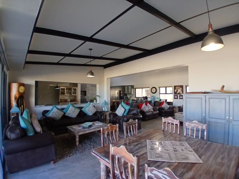 Spacious open-plan living and dining area featuring exposed ceiling beams, tiled flooring, and a convenient pass-through window connecting to the kitchen.