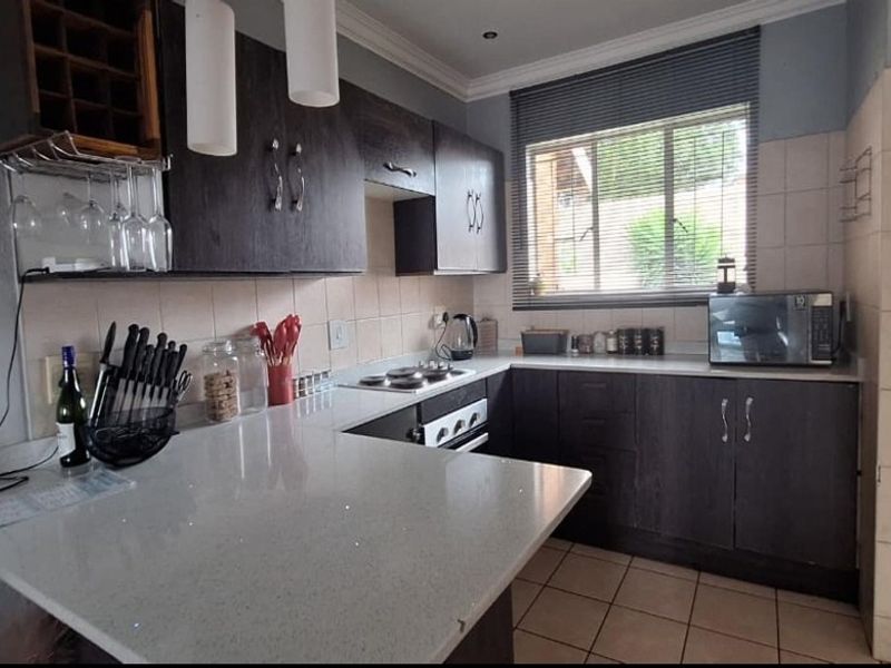 A functional kitchen featuring dark cabinetry, stone countertops, a built-in hob and oven, and tiled flooring with a window for natural light.