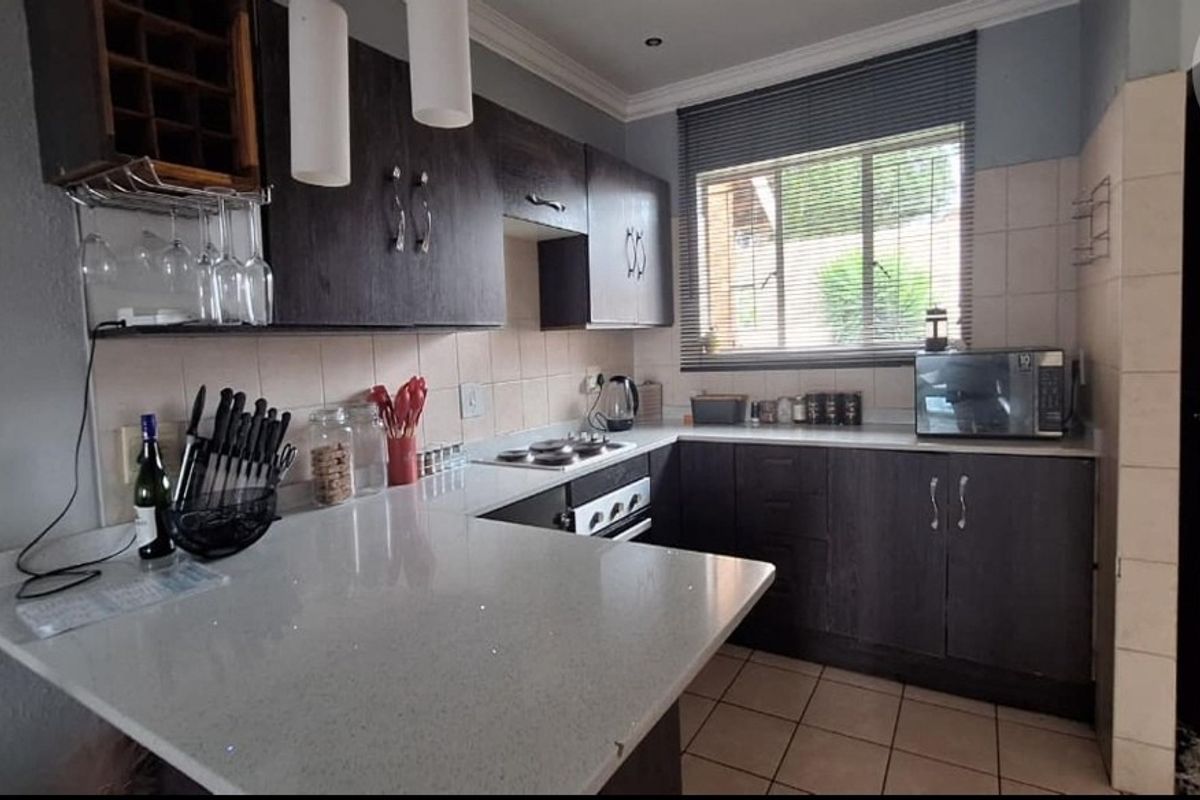 A functional kitchen featuring dark cabinetry, stone countertops, a built-in hob and oven, and tiled flooring with a window for natural light.