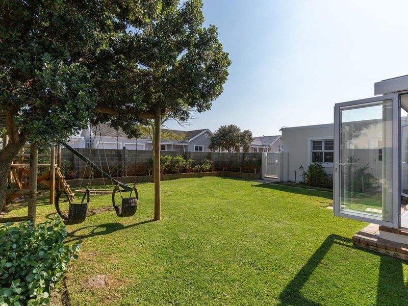 A well-maintained rear garden featuring a lush lawn, boundary wall, and direct access to the home through a glass sliding door.