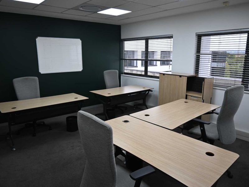 A professional office space featuring recessed ceiling lighting, dark accent wall, carpeted flooring, and large windows with venetian blinds.